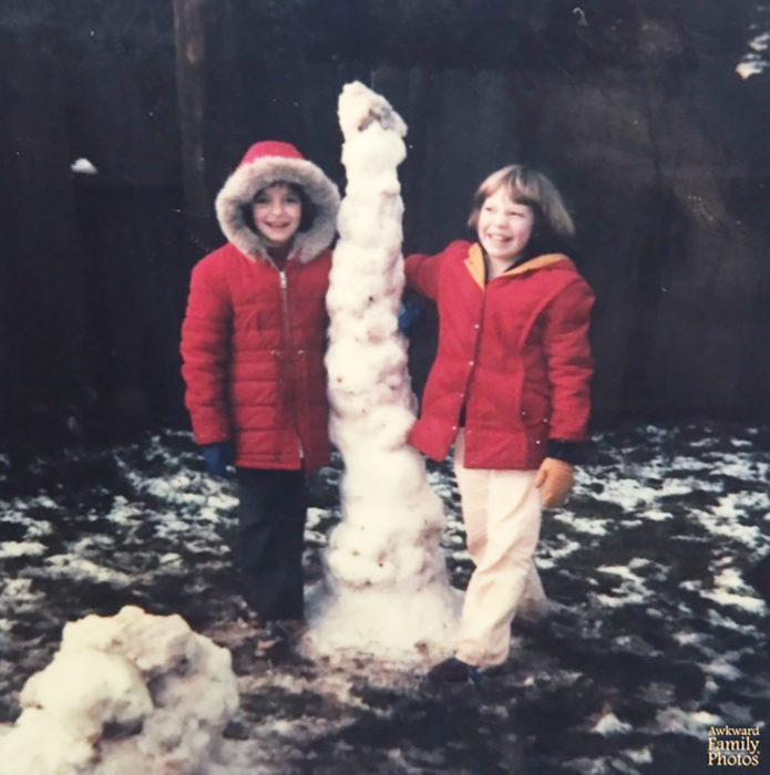 dos niños posando con una escultura de nieve que se ve perversa