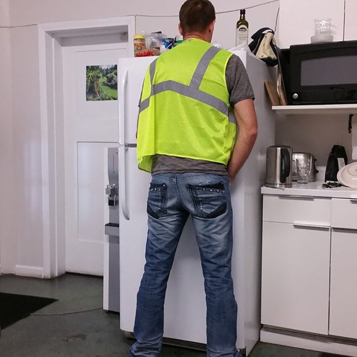 hombre con chaleco fluorescente tratando de orinar en un refrigerador