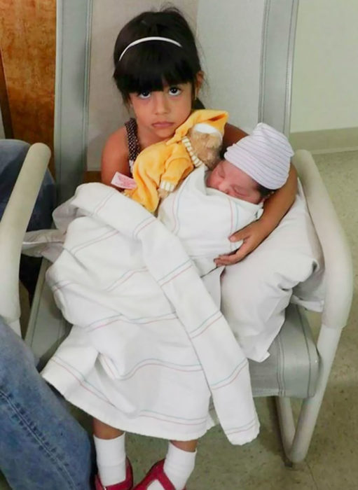 niña molesta cargando a su hermanito recién nacido
