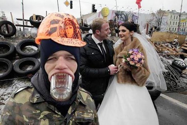 hombre con casco y vaso de vidrio en la boca frente a una pareja de casados
