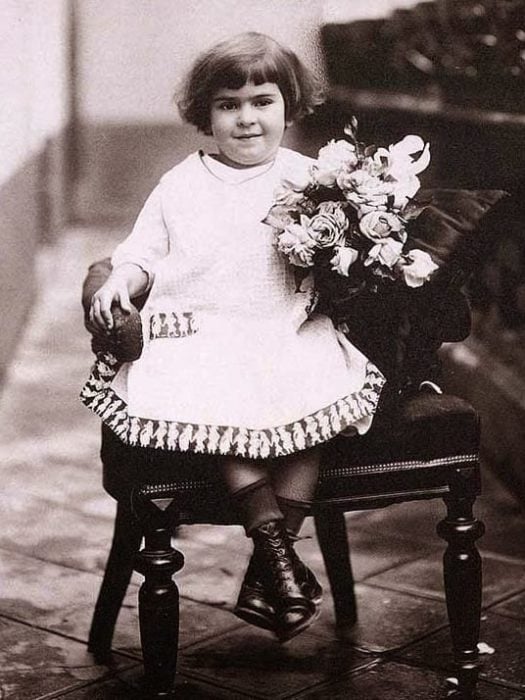 Frida Kahlo de niña sentada en una silla con flores en la mano