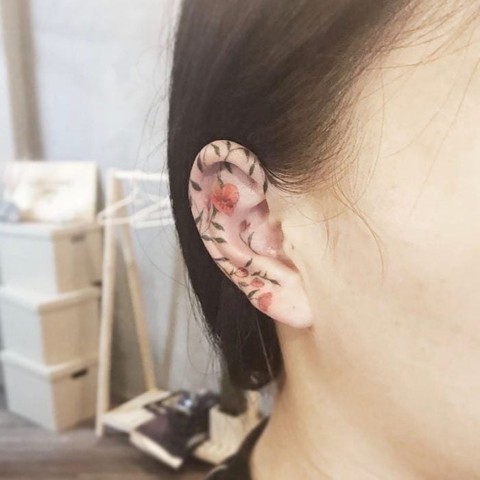 Tatuaje de flores rojas con ramas en el oido 