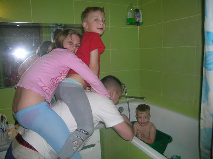 papá bañando a un niño mientras carga otros dos