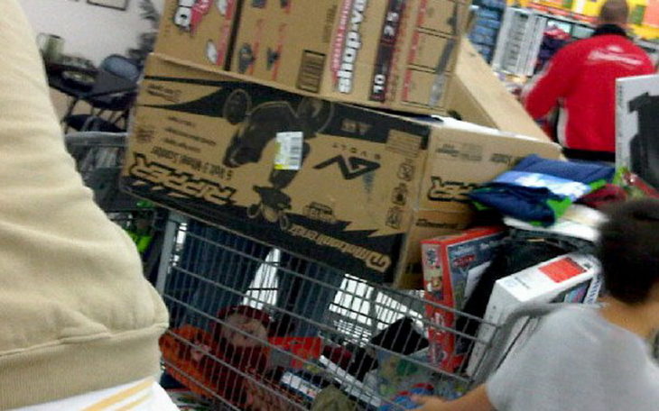 Niño dormido en carrito de compras y arriba va lleno de cajas