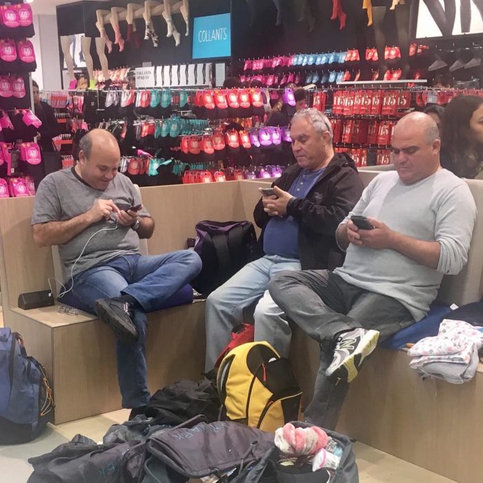 Hombres con el celular mientras sus esposas compran