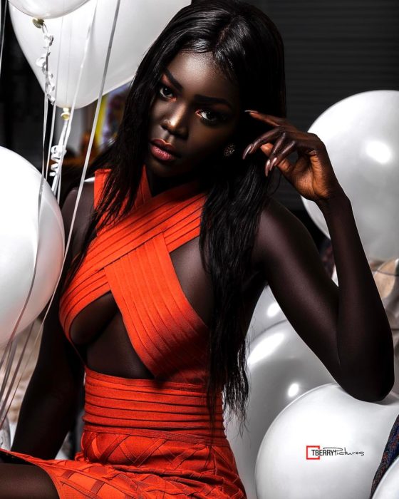 Modelo negra con vestido naranja y globos blancos alrededor