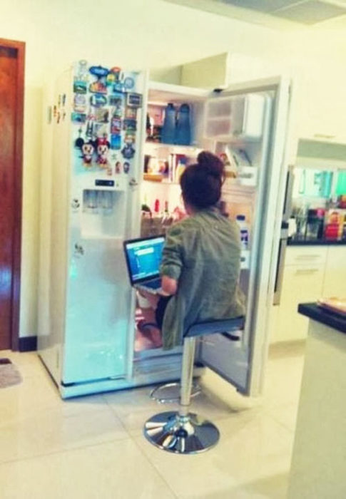 Chica con la computadora en las piernas sentada frente al refrigerador