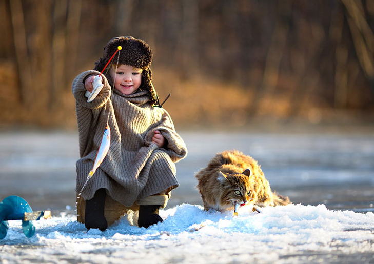 niño pescando en el hielo un gato a su lado