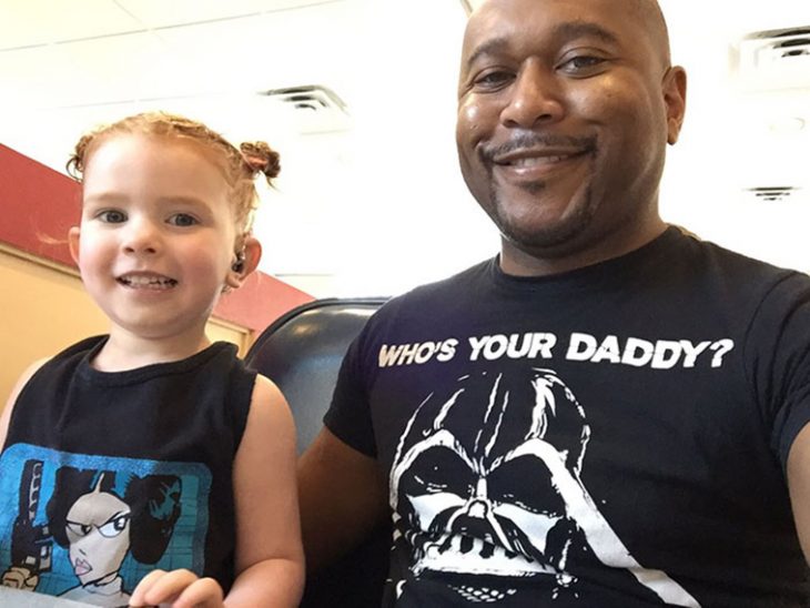 hombre con playera negra sonrriendo aun lado una niña