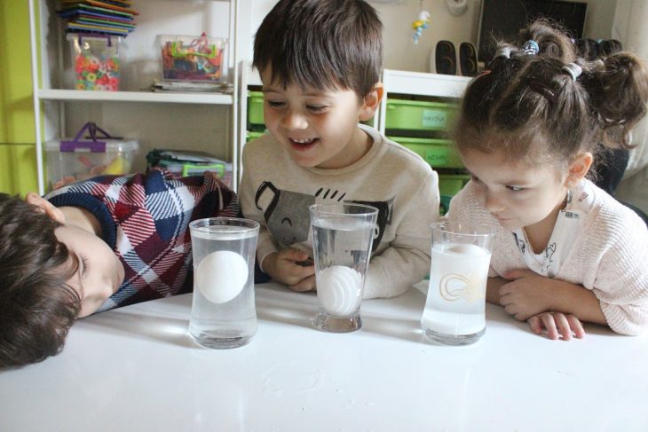 niños mirando un experimento en vasos con huevos