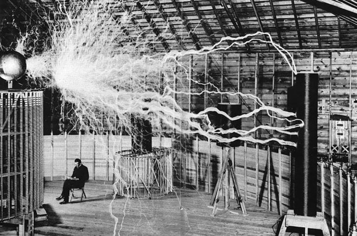 Nikola Tesla sentado en su laboratorio con la conocida Bobina de Tesla