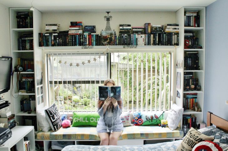 estanterías enmarcando una ventana y chica sosteniendo un libro