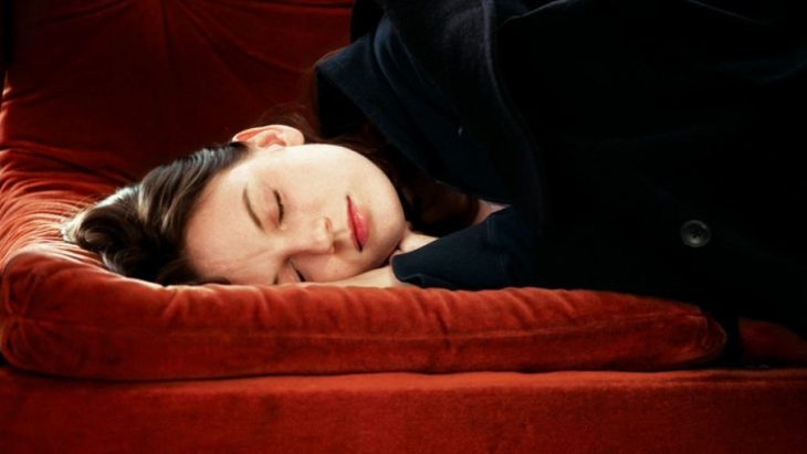 Mujer con blusa negra recostada en un sillón rojo 