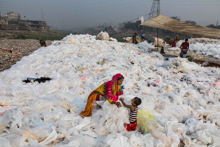 mujer con niño en medio de un basurero de plástico 