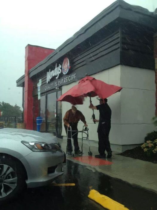 Empleado cubre de la lluvia a un anciano con una sombrilla de mesa