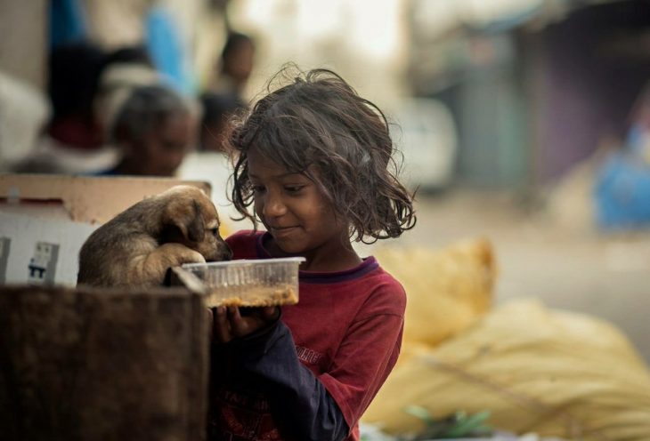 niña pobre alimentando a un perro 