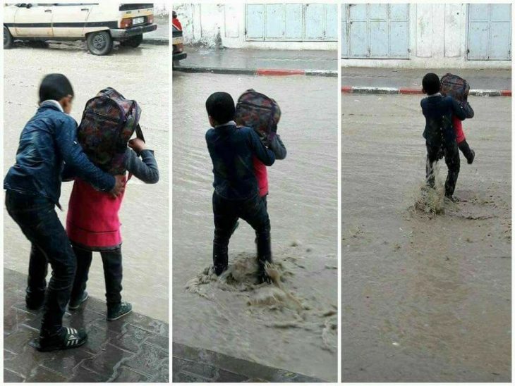 niño ayuda a hermana a cruzar calle inundada 