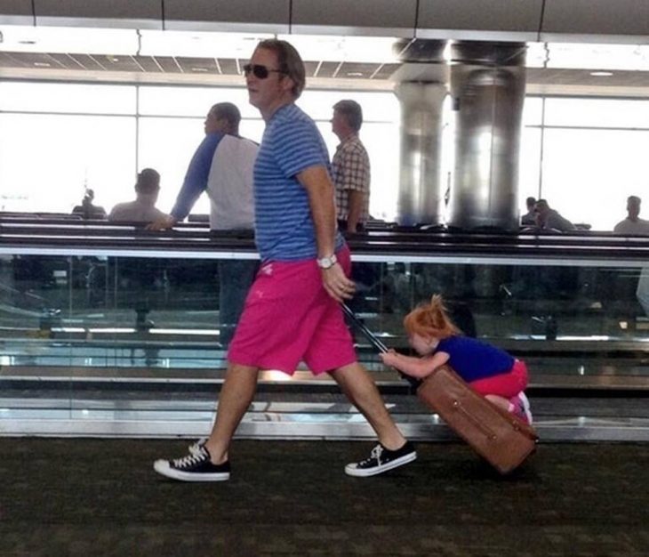 hombre cargando una maleta que a su vez está cargando a una niña 