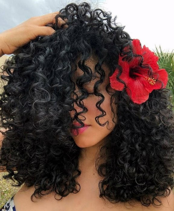 mujer con el pelo rizado y una flor roja